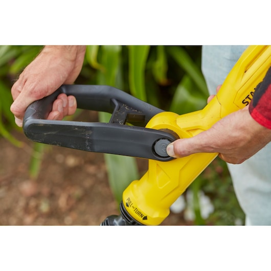 Close-up van het handvat van de STANLEY SFMCST933B grastrimmer met gele en zwarte details, buitenomgeving.