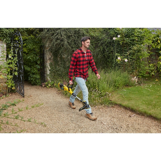 STANLEY SFMCST933B grastrimmer gedragen door een persoon op een tuinpad.