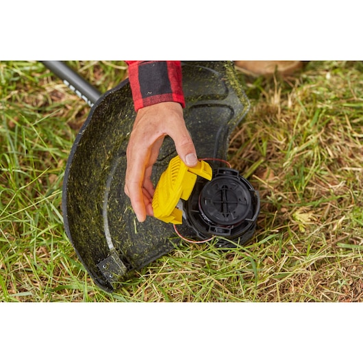 STANLEY SFMCSTB933B grastrimmer close-up, hand bevestigt gele kap op trimmerkop op gras.