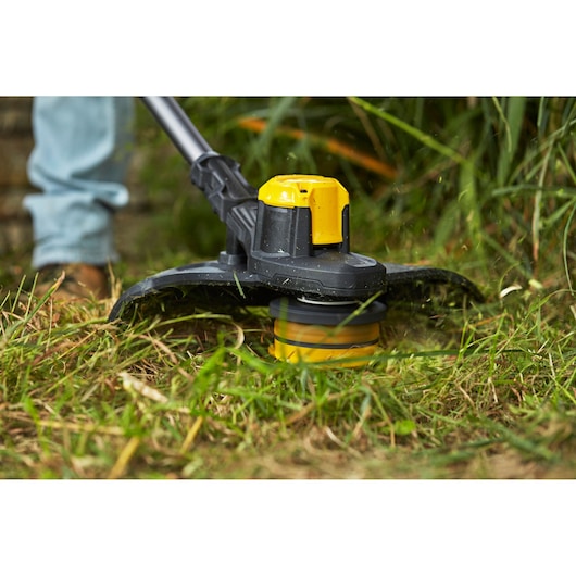 Foto van de STANLEY SFMCSTB933M grastrimmerkop die gras snijdt, close-up buitenzicht.