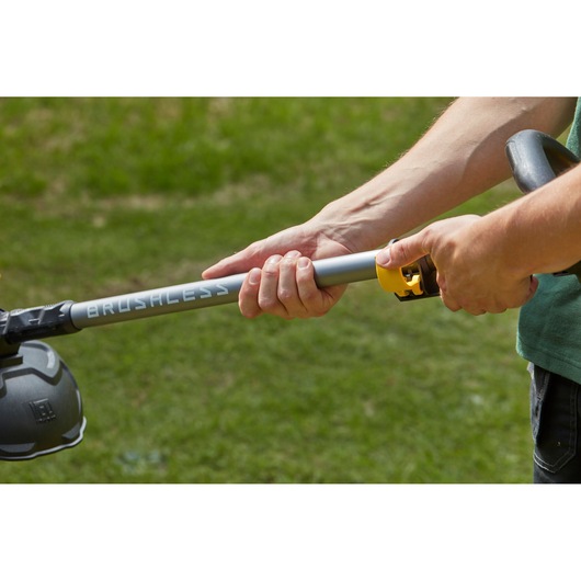Foto van handen die de steel van de STANLEY SFMCSTB963B brushless grastrimmer op gras aanpassen.