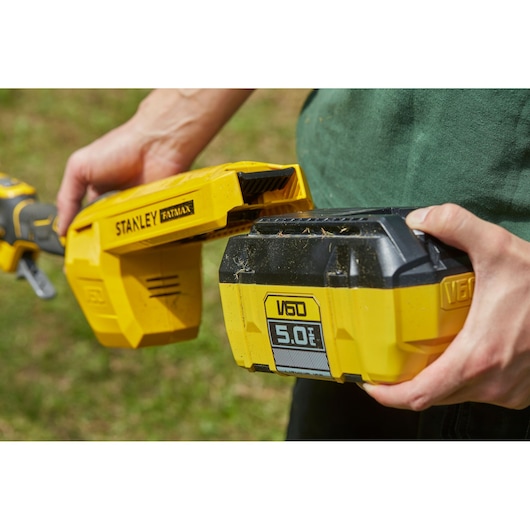 Foto van de gele STANLEY SFMCSTB963B V60 5.0Ah accu die in een STANLEY FATMAX gereedschap buitenshuis wordt geplaatst.