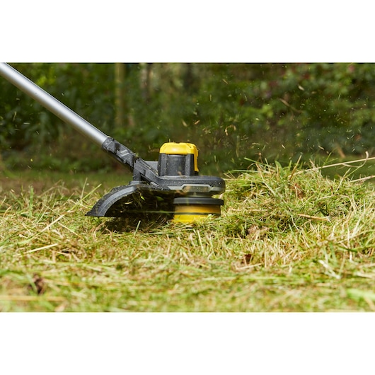 Foto van STANLEY SFMCSTB963B grastrimmer in gebruik bij het maaien van gras buiten.