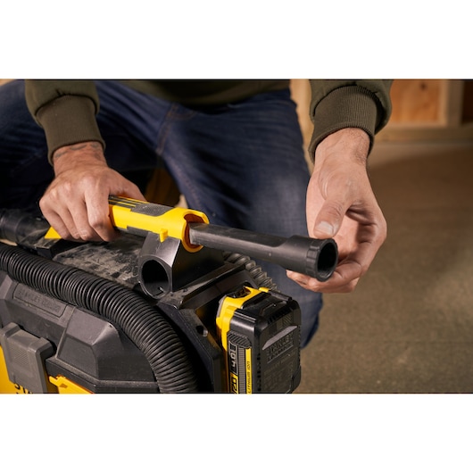 Photo de mains fixant un tuyau à l’aspirateur STANLEY SFMCV002B, vue rapprochée du connecteur et de la batterie.