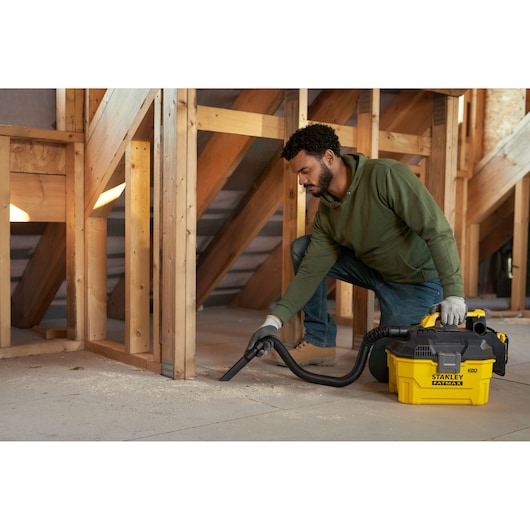 Photographie de l’aspirateur eau et poussière STANLEY SFMCV002B utilisé pour nettoyer la poussière dans un grenier en bois.