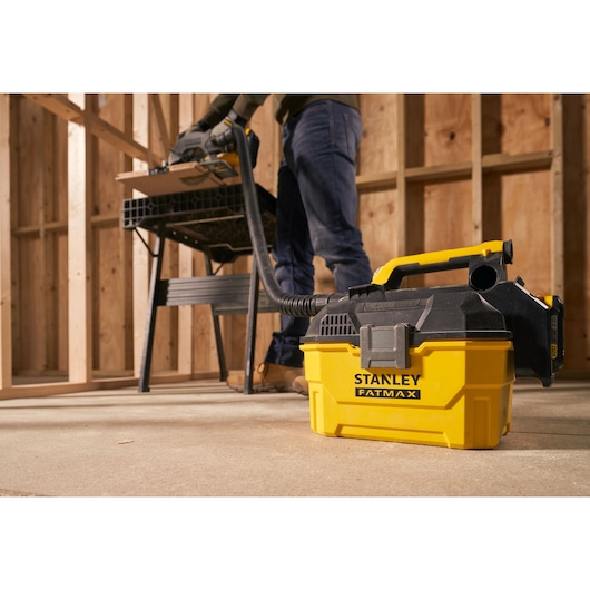 Aspirateur portable STANLEY SFMCV002B jaune et noir dans un atelier, connecté à un outil.