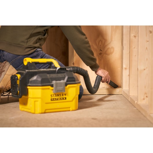 Aspirateur humide/sec STANLEY SFMCV002B jaune et noir, utilisé pour nettoyer un coin de sol en bois.
