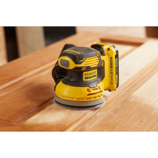 STANLEY SFMCW220B ponceuse sans fil sur surface en bois, jaune et noire, angle latéral rapproché.