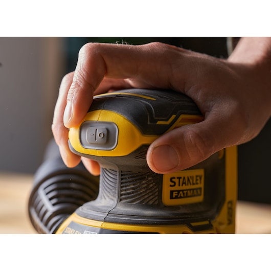 Photo de la ponceuse STANLEY SFMCW220B, gros plan d'une main sur le bouton d'alimentation, jaune et noir.