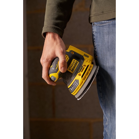 Foto van STANLEY SFMCW220D1S snoerloze schuurmachine in hand, geel met zwart, close-up.