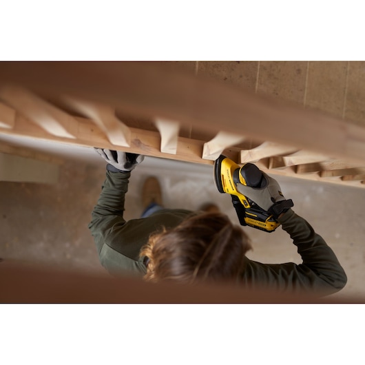 Foto van persoon met handschoenen die STANLEY SFMCW221D1S accu schuurmachine op houten leuning gebruikt.