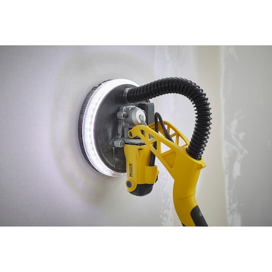 STANLEY SFMEE500S gipsplaat schuurmachine met LED-ringlicht schuurt een muur, zijaanzicht.