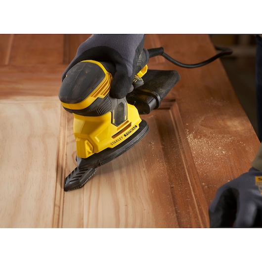 Photographie de la ponceuse STANLEY SFMEW210S utilisée sur une surface en bois, angle rapproché montrant la poussière.