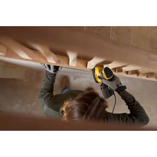 Personne utilisant la ponceuse STANLEY SFMEW210S sur une rampe d’escalier en bois, vue de dessus.