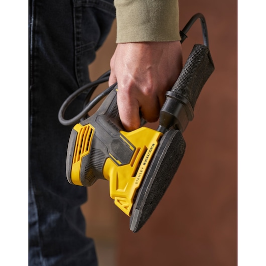 Photo de la ponceuse électrique STANLEY SFMEW210S en main, design noir et jaune, gros plan du produit.