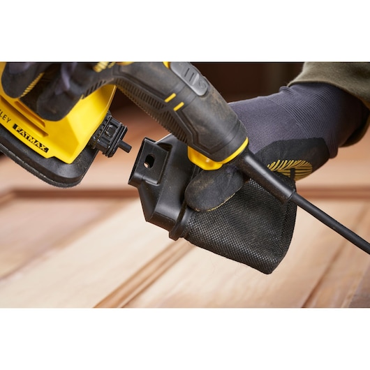 Stanley SFMEW210S ponceuse gros plan, fixation du sac à poussière, outil jaune et noir en utilisation.