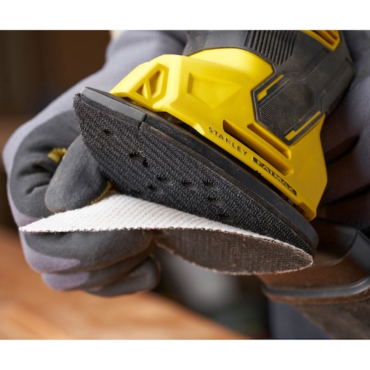 Photo de ponceuse STANLEY SFMEW210S en gros plan avec pad abrasif fixé, design jaune et noir.