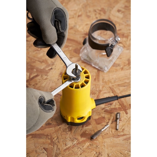 Assemblage de défonceuse STANLEY ST55 avec clés et mains gantées, gros plan sur l’outil et accessoires sur surface bois.