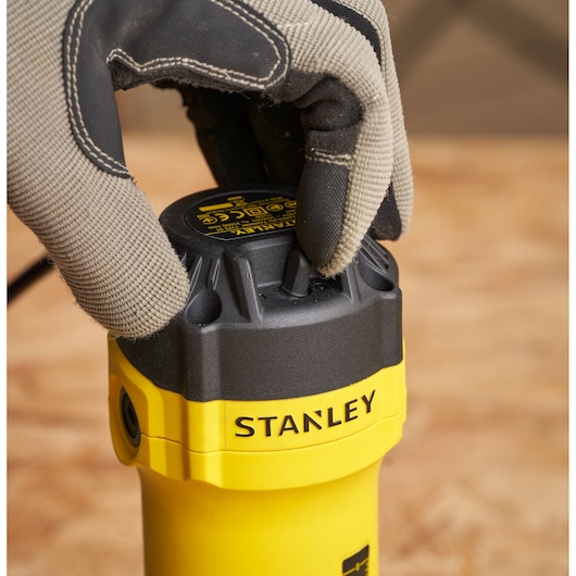 Photo du STANLEY ST55, gros plan sur l'outil avec une main gantée ajustant le bouton noir, corps jaune visible.