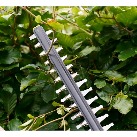 STANLEY STCHT8255B heggenstrimmerblad in actie, close-up met groene bladeren op de achtergrond.