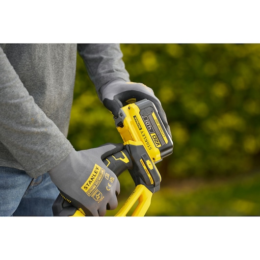STANLEY STCHT8255B handschoenen gedragen bij het vasthouden van een gele STANLEY powertool buiten.