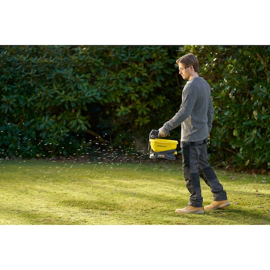 Personne utilisant un épandeur STANLEY STCOE300B sur de l’herbe dans un jardin.