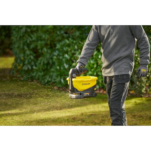 STANLEY STCOE300B épandeur en utilisation extérieure, outil jaune et noir à main dispersant du matériel sur l’herbe.