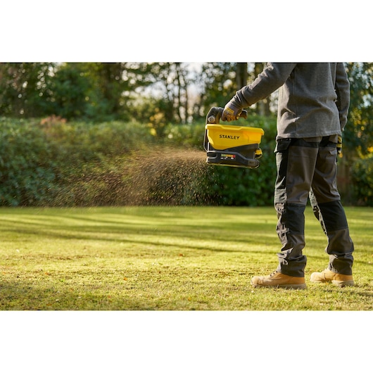 Stanley STCOE300B épandeur portatif utilisé en extérieur pour répartir du matériau sur une pelouse.