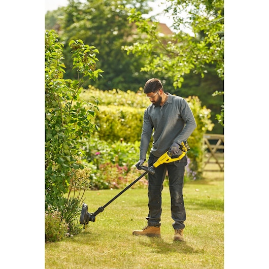 Photo d'une personne utilisant un coupe-bordure STANLEY STCST933B dans un jardin, tenant l’outil jaune et noir sur l’herbe.