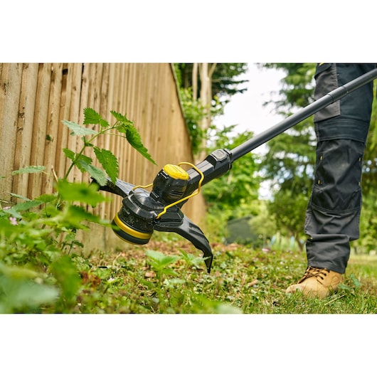 STANLEY STCST933B coupe-bordures en gros plan utilisé pour couper des mauvaises herbes le long d'une clôture en bois.