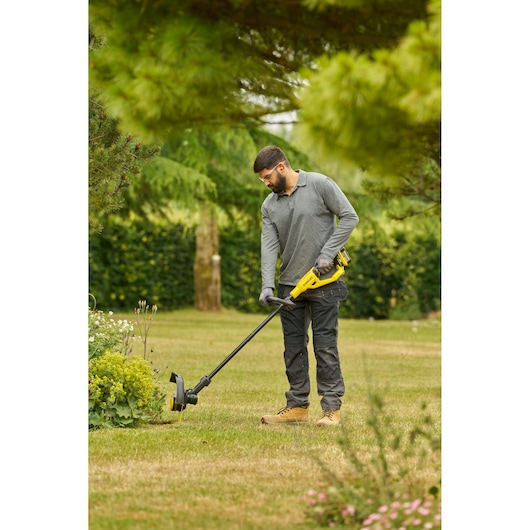 STANLEY STCST933B coupe-bordures en utilisation, personne taillant le bord de la pelouse avec outil sans fil jaune et noir.
