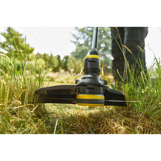 STANLEY STCST933B coupe-bordures en utilisation, vue en contre-plongée gros plan sur la tête de coupe travaillant l’herbe haute.