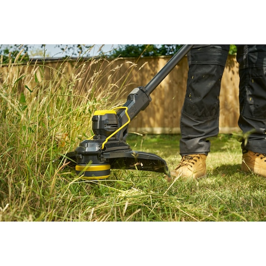 STANLEY STCST933B coupe-bordures utilisé en extérieur pour couper de l’herbe haute près d’une clôture en bois.