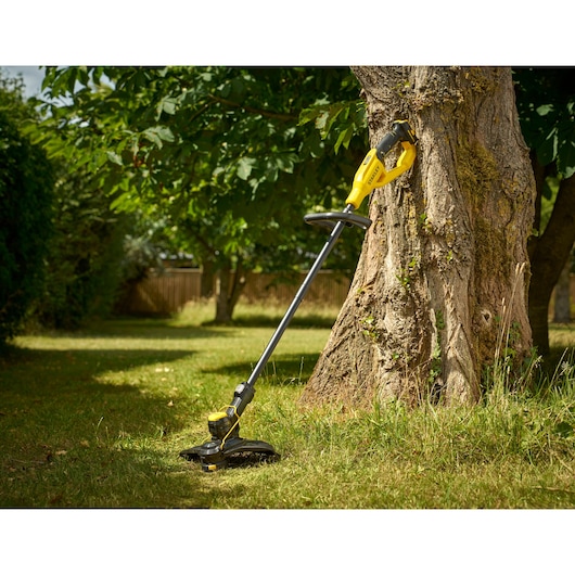 STANLEY STCST933B coupe-herbe jaune et noir appuyé contre un arbre dans un jardin.
