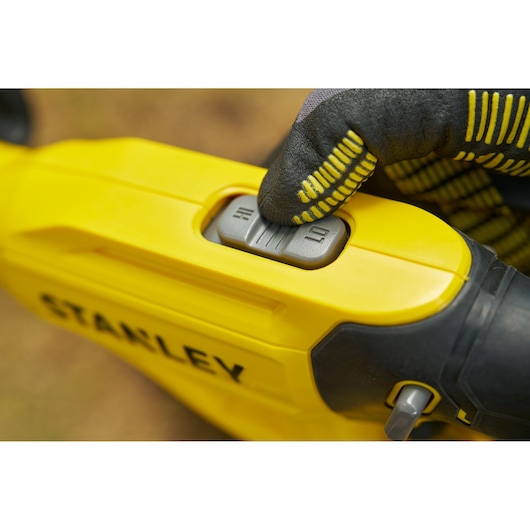 Stanley STCST933B bouton de commande d’outil électrique en gros plan, corps jaune et gant appuyant.