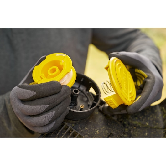 STANLEY STCST933B assemblage de bobine de coupe-bordures, photo gros plan de la bobine jaune et du couvercle dans des mains gantées.