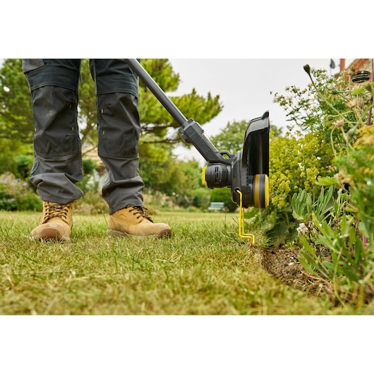 STANLEY STCST933M1 coupe-bordures en utilisation, vue latérale, taillant le bord de la pelouse près des plantes.