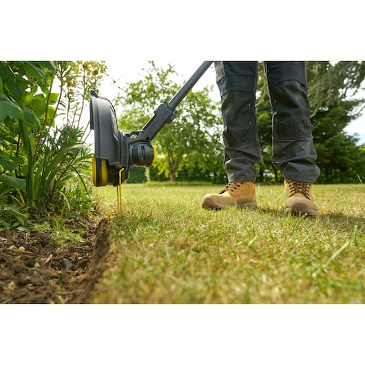 STANLEY STCST933M1 coupe-bordures en utilisation, gros plan sur la lame et les bottes sur l'herbe.