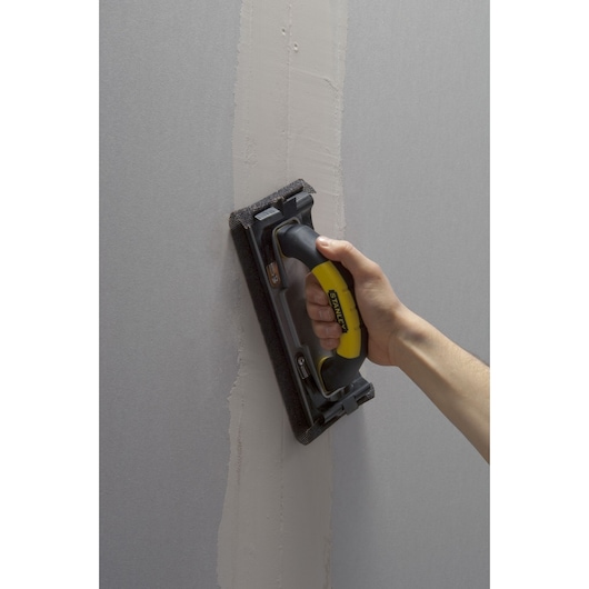 Foto van STANLEY STHT0-05927 handschuurblok met zwarte en gele greep op een muur.