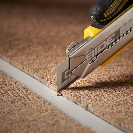STANLEY STHT0-11825 couteau utilitaire découpant une moquette marron, gros plan sur la lame précise.