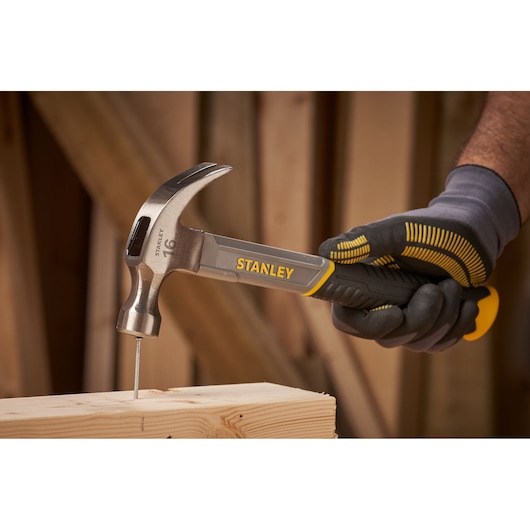 Foto van STANLEY STHT0-51309 klauwhamer die een spijker in hout slaat, vastgehouden in een gehandschoende hand.