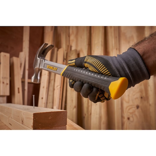 STANLEY STHT0-51309 klauwhamer vastgehouden door een gehandschoende hand, bij spijker en hout, werkplaats.
