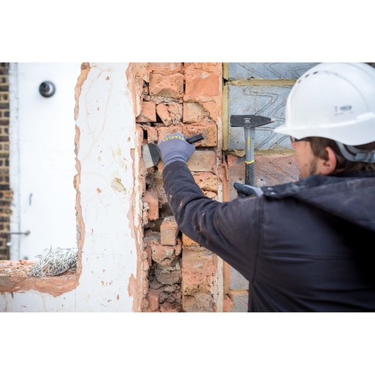 Ciseau STANLEY STHT0-51910 utilisé sur mur en briques par un ouvrier avec gants et casque.