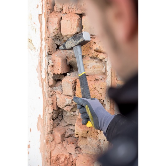 Marteau STANLEY STHT0-51910 avec poignée noire et jaune utilisé sur mur en briques abîmé.