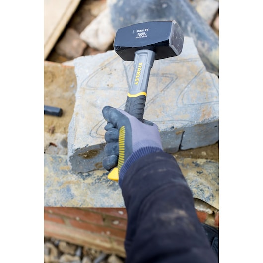 Marteau massette STANLEY STHT0-54128 avec manche jaune et noir tenu par une main gantée sur chantier en pierre.