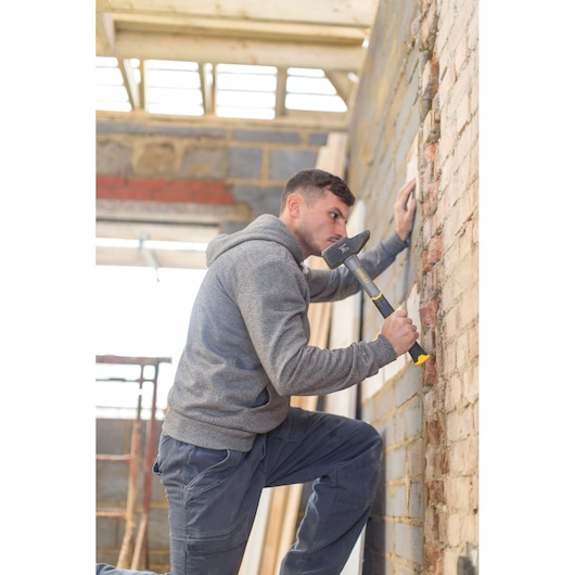 Photo d'une personne utilisant une masse STANLEY STHT0-54157 sur un mur en briques sur un chantier.