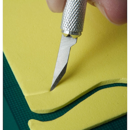 Couteau de précision STANLEY STHT0-73872 découpant de la mousse jaune sur surface verte, vue rapprochée.