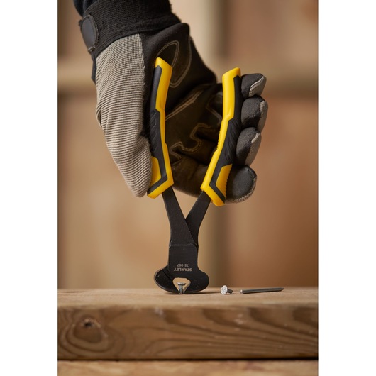 Photo de STANLEY STHT0-75067 pince coupe-bout jaune tenue par une main gantée, retirant un clou du bois.