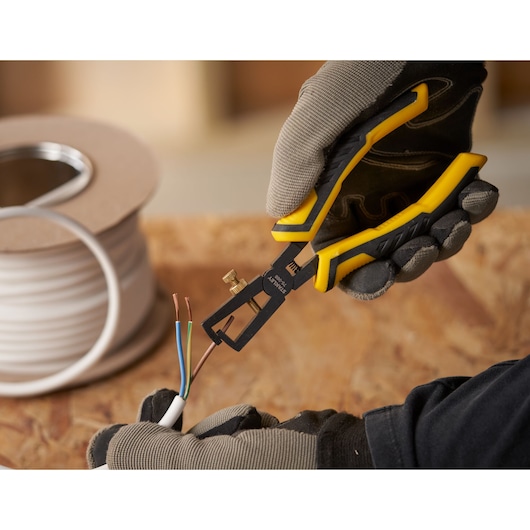 STANLEY STHT0-75068 pince à dénuder tenue par une main gantée, dénudant des fils colorés sur bois.