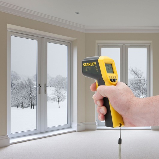 Stanley STHT0-77365 thermomètre infrarouge tenu en main, mesure la température d'une fenêtre en intérieur.